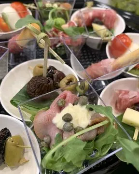 Antipasti in kleine bakjes: rolletjes vleeswaren, olijven, kappertjes en rucola