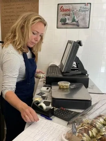 Elke den Hollander aan de toonbank van Deli Megusto, met haar bestellijst en de weegschaal