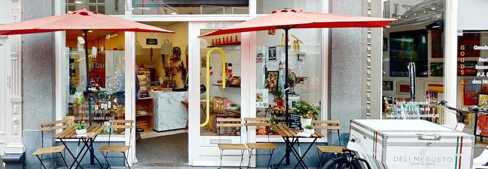 De winkel van Deli Megusto aan de Kleiweg 91: rode parasols, terrastafeltjes, de open deur en de bakfiets van de winkel
