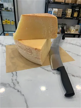 Een groot stuk parmezaan met een kaasmes op marmer