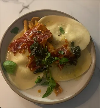 Bord met verse ravioli, krokante ham, salie en basilicum