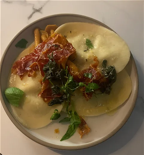Bord met verse ravioli, krokante ham, salie en basilicum