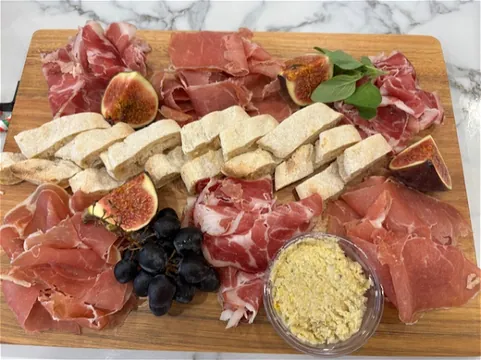 Plank met Italiaanse vleeswaren, vijgen, druiven, brood en tapenade op marmer